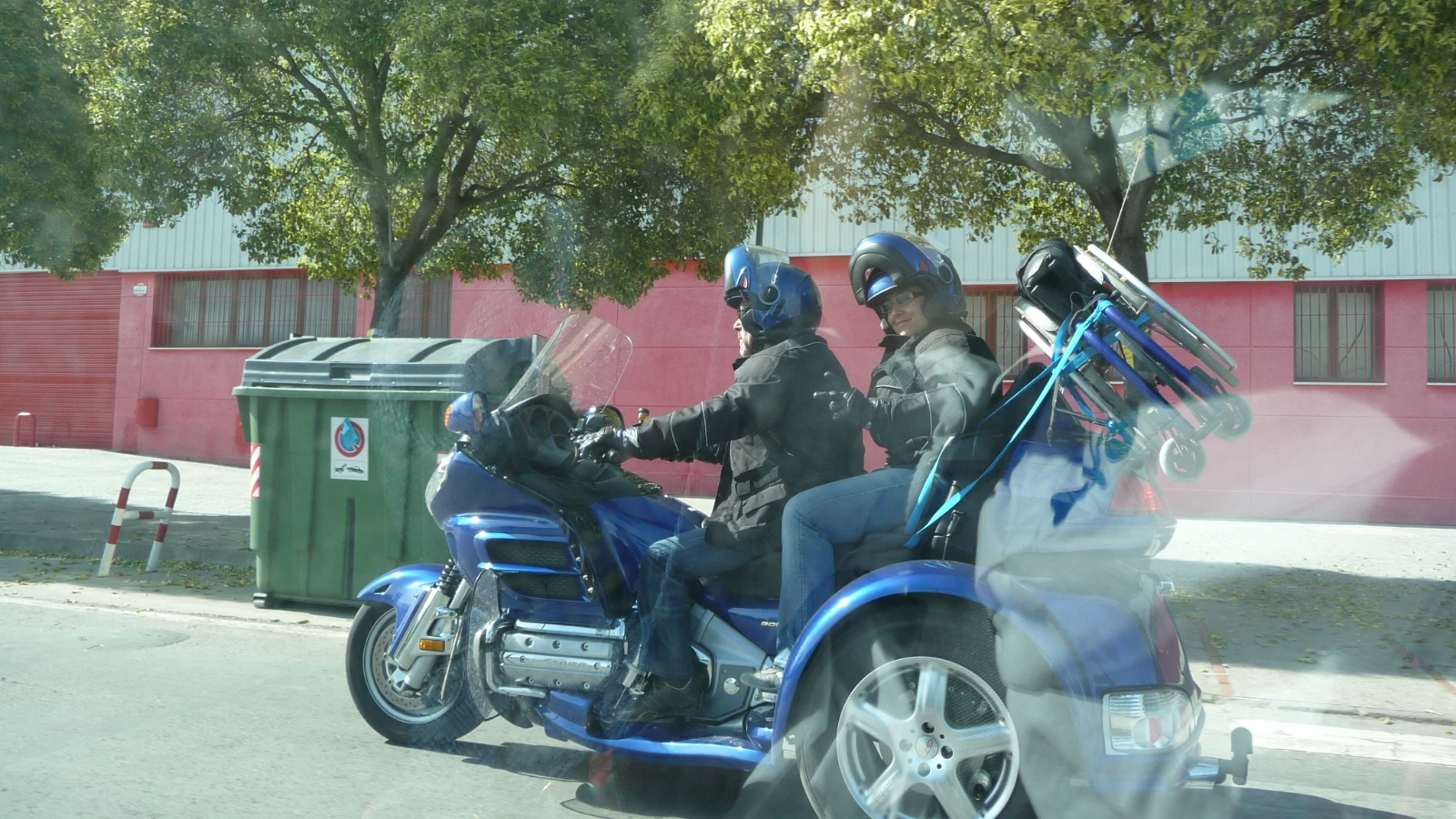 Blaues Honda-Gold-Wing-Trike mit Fahrer und Beifahrerin in Jacken und Helmen auf einer Straße in Jerez, hinten ein festgeschnallter Rollstuhl, fotografiert durch eine Autoscheibe